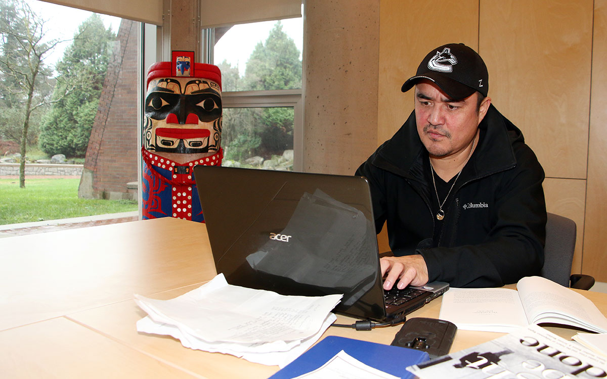 Malcolm Stewart, of the Nisga'a Nation, is a student in the Justice and Public Safety Certificate program at JIBC. Here he works on an essay in JIBC's Aboriginal Gathering Place as a house post by Nisga'a artist Mike Dangeli looks on. 