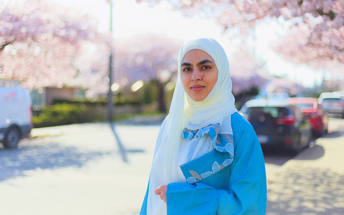 Mona Zafar on street lined with cherry blossom trees.