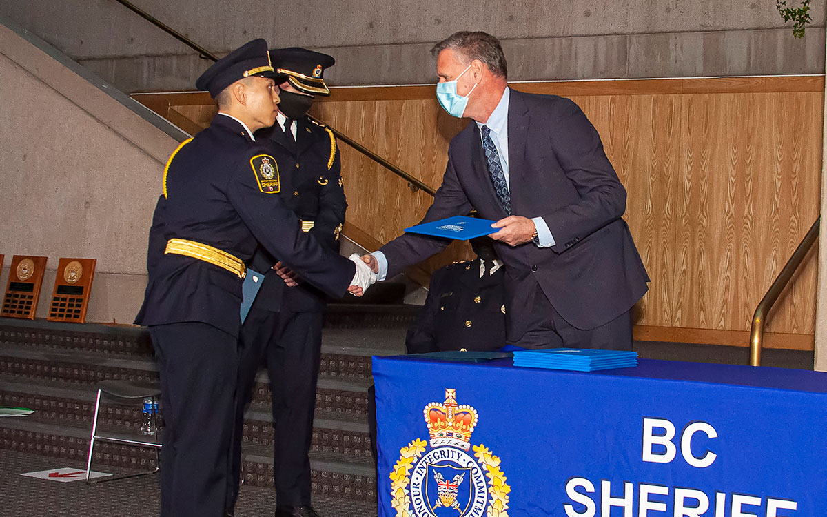 JIBC President and CEO Dr. Michel Tarko presents certificate to sheriff recruit at graduation ceremony at Vancouver Law Courts.