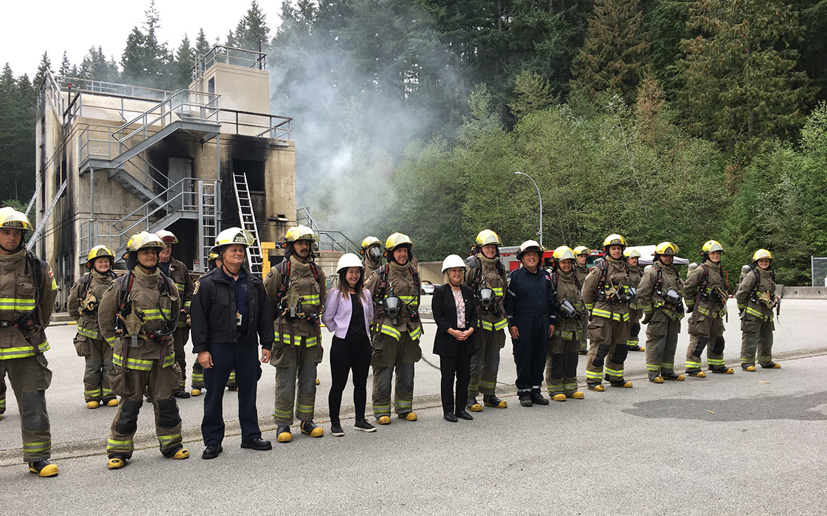 Advanced Education and Skills Training Minister Anne Kang and Maple Ridge-Pitt Meadows MLA Lisa Beare pose with firefighting students in front of the burn building at Maple Ridge campus.