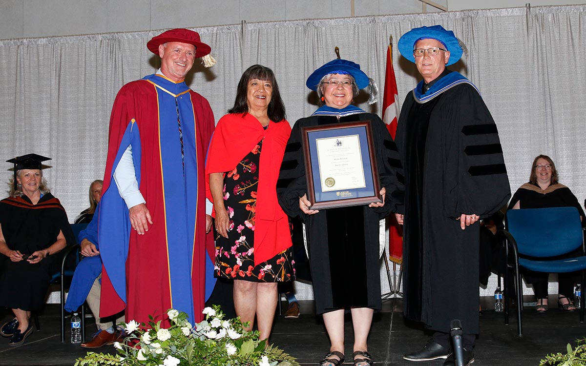 JIBC President and CEO Dr. Michel Tarko, Qayqayt Chief Rhonda Larrabee, and JIBC Board Chair Dr. Stephen Gamble, with Orange Shirt Day founder Dr. Phyllis Webstad, holding a framed certificate,, after she was conferred an honorary degree at the 2023 convocation ceremony.