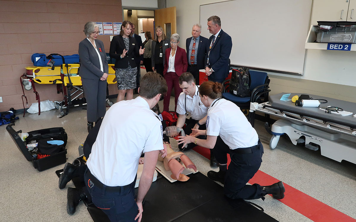 Paramedic students perform a training exercise while group of dignitaries observe.