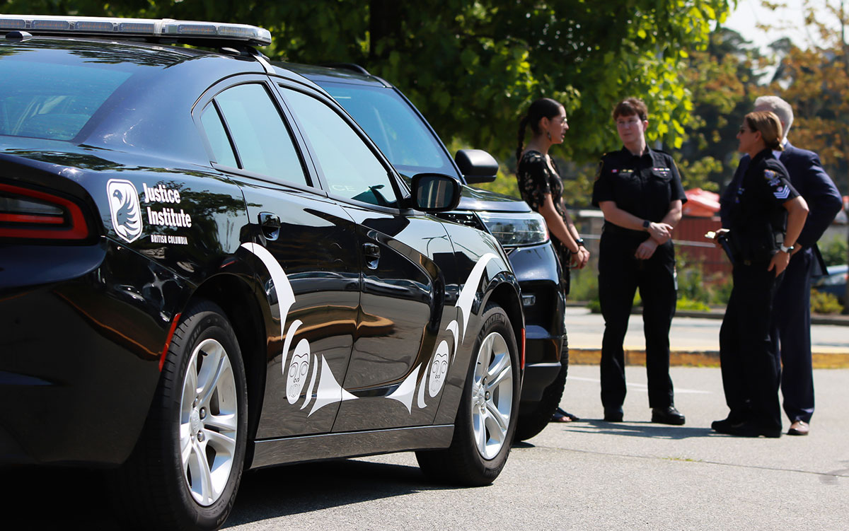 JIBC Police Academy car with new Indigenous artwork in foreground while the artist speaks with academy staff in background.