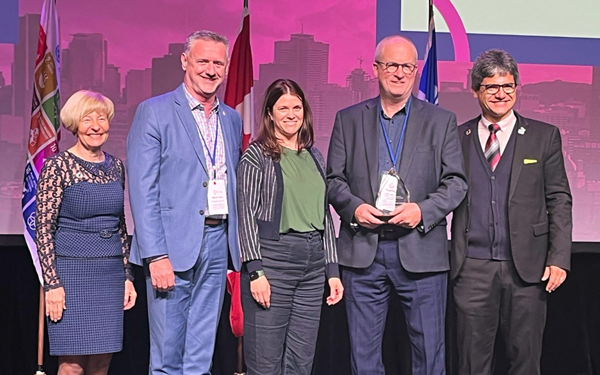 Group of five people stand posing with award held by one of the men. 