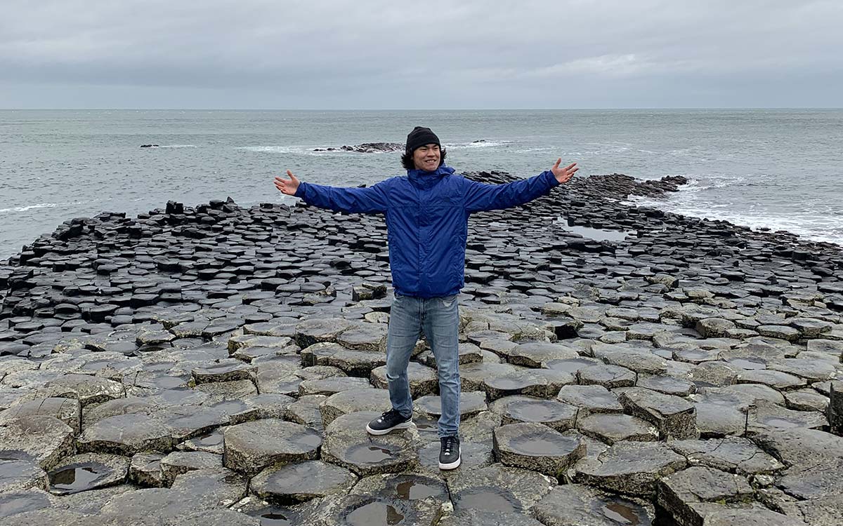 Man stands with arms outstretched at Giant's Causeway in Northern Ireland.
