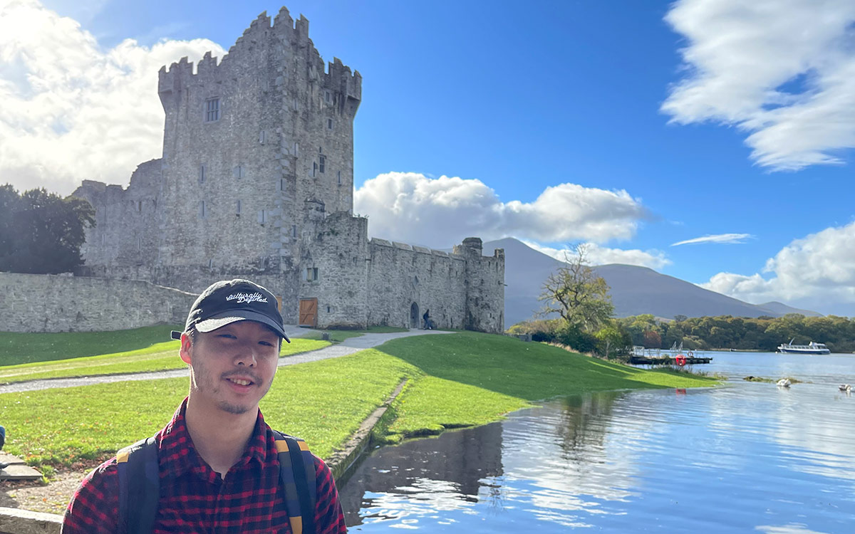 Male student wearing ball cap poses against ruins of a castle in Ireland.