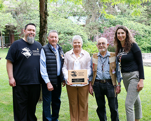 Three men and a woman pose with a plaque held by a second woman in the centre.