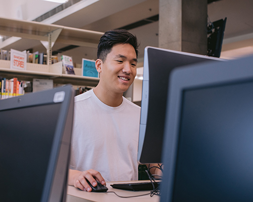 Young man with dark hair wearing white t-shirt looks at computer screen.
