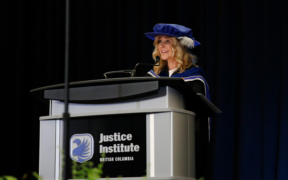 Woman in black graduation robe and blue doctorate’s cap speaks at podium.