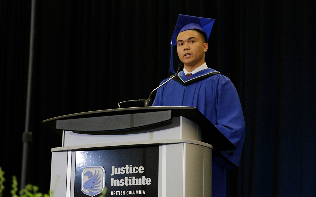 Man in blue graduation gown and cap speaks at a podium.