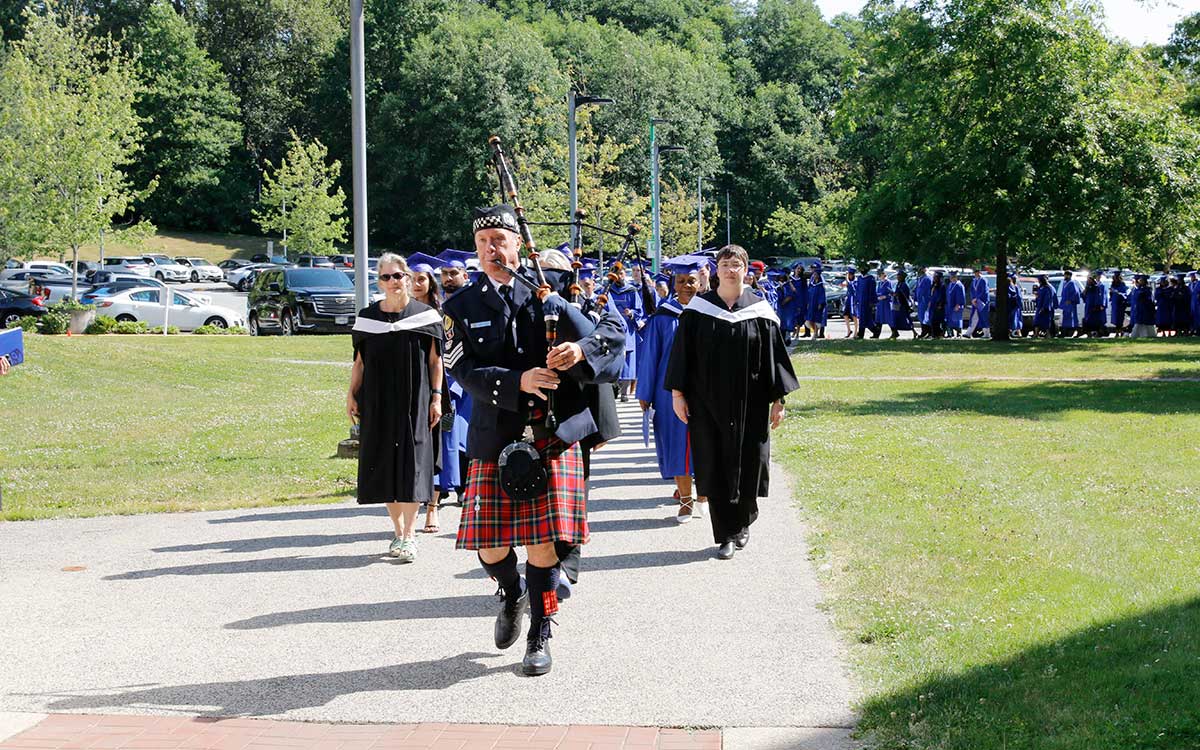 A bagpiper leads a procession of JIBC graduates in blue gowns into the convocation ceremony.