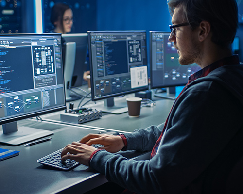 A person sitting at a desk in front of three computer monitors