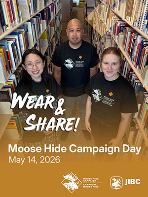 A man and two women stand between bookshelves wearing black t-shirts and pins from the Moose Hide Campaign. Overlaid is "Wear & Share!"