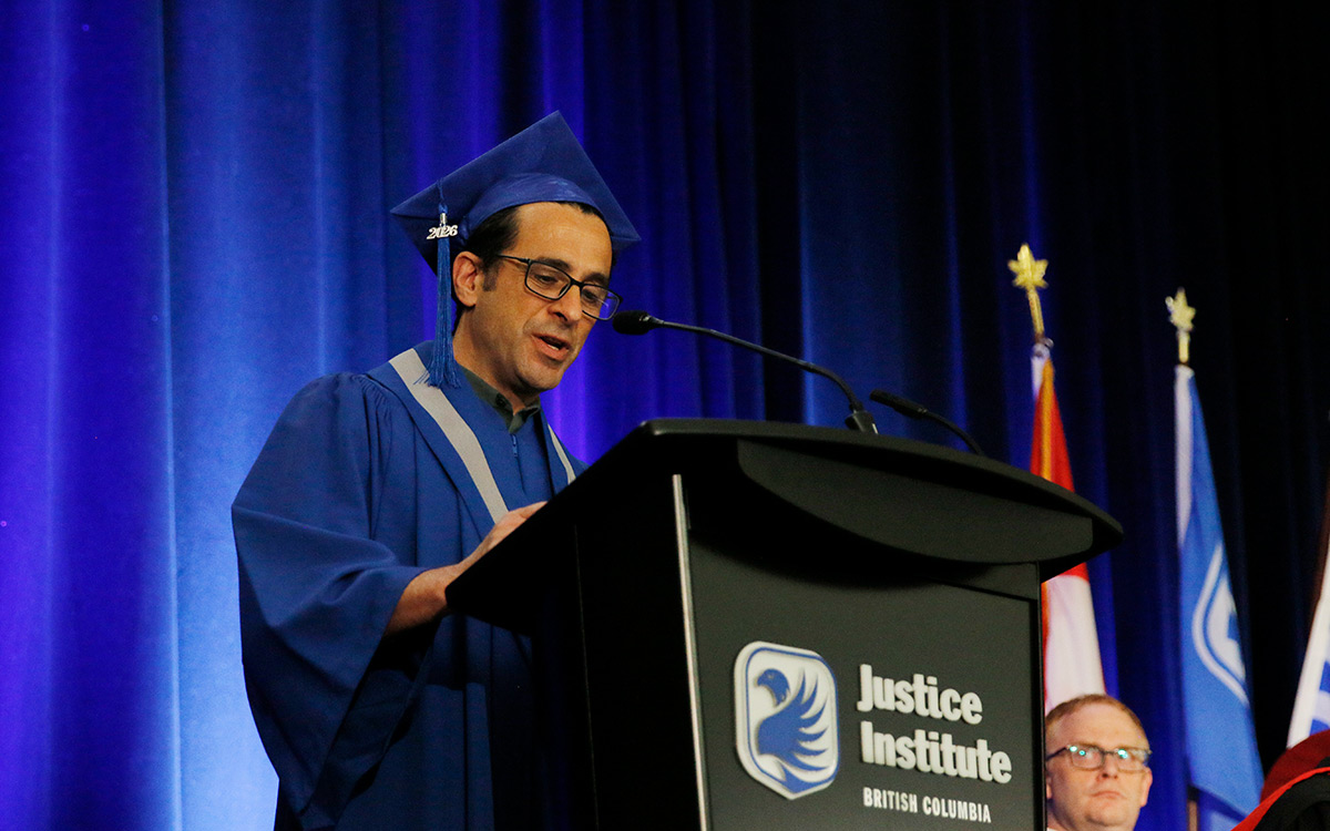 Man in blue graduation gown speaks at podium.