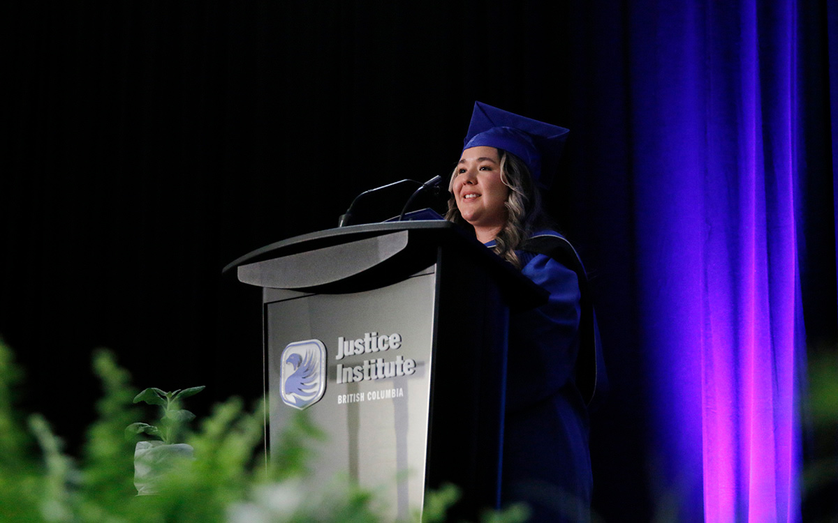 Graduate in blue gown speaks at podium.