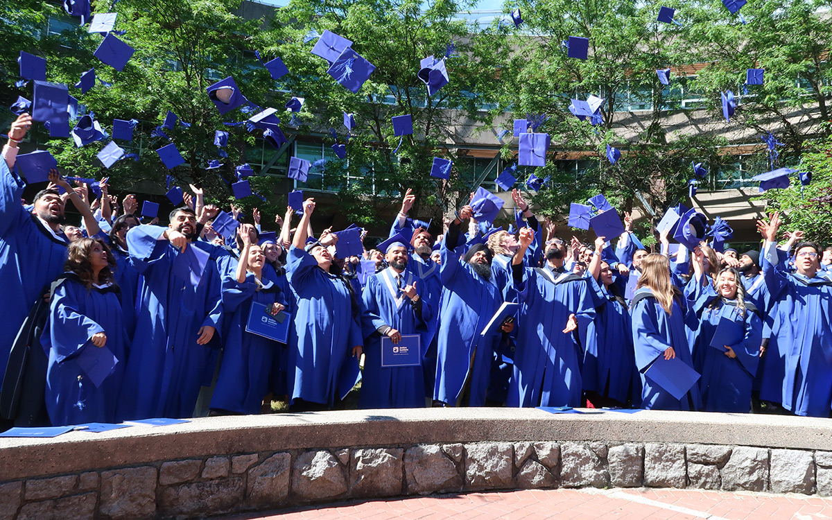 Graduates in blue gowns toss their caps.