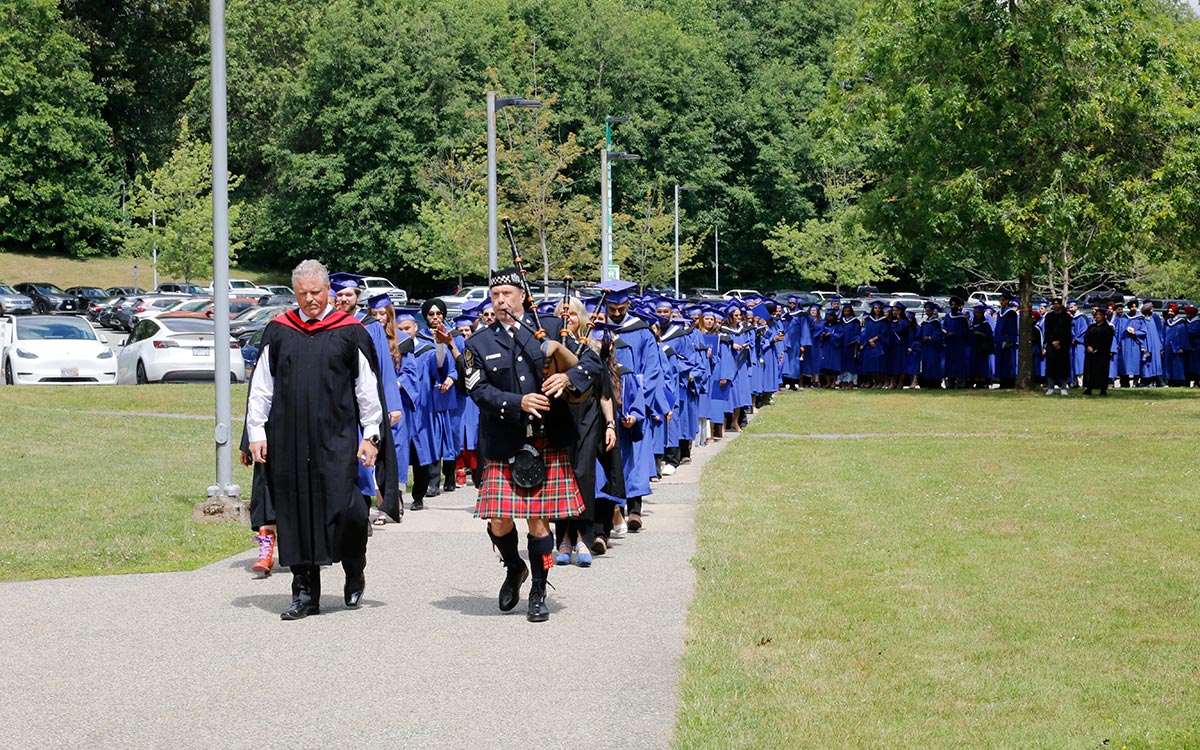 Bagpiper leads march of graduates in blue gowns.
