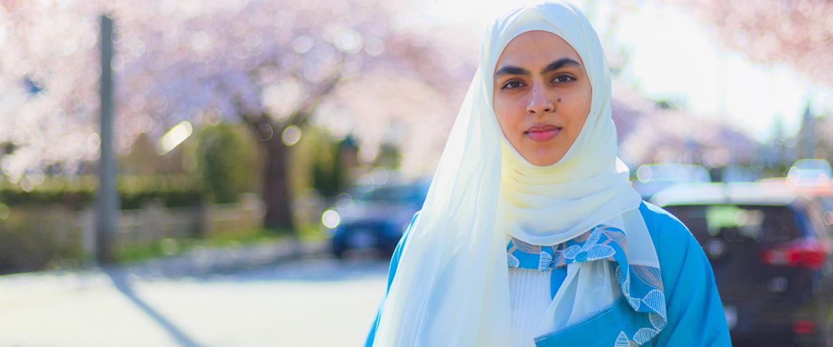 Mona Zafar standing on street lined with cherry blossom trees.