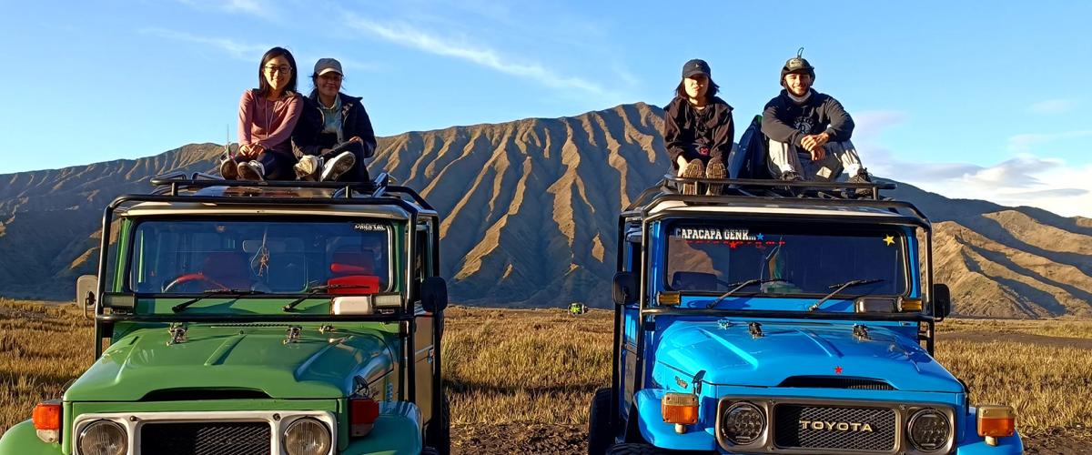 Four students sit atop jeeps with Indonesian mountains in background.