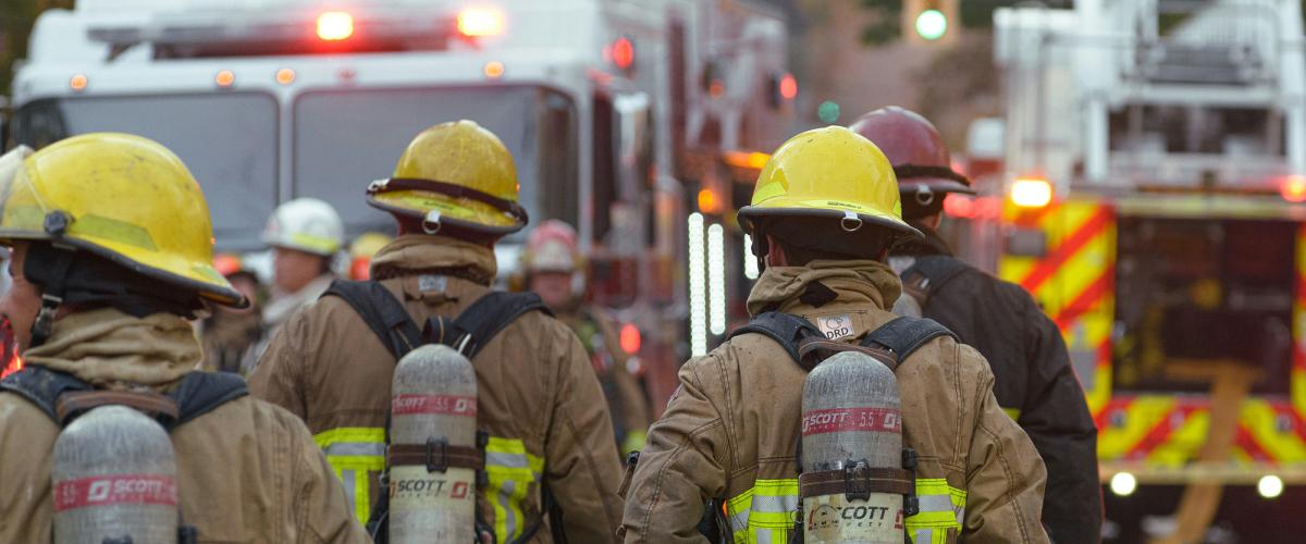 Rear view of firefighters in turnout gear walking towards fire truck..