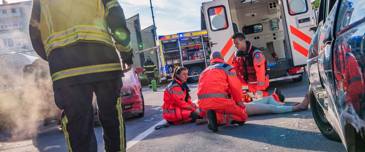 Firefighter walking towards three paramedics treating patient on ground behind ambulance.