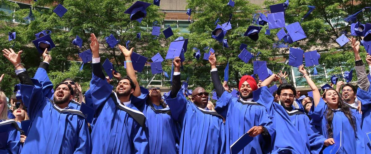 JIBC graduates in blue gowns toss their blue grad caps in the air.
