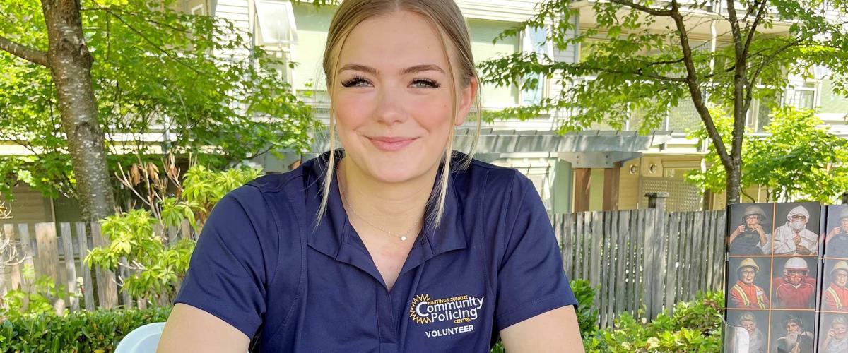 Woman sits at a table outdoors wearing golf shirt that says "community policing volunteer."