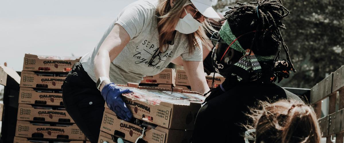Woman passes crate of food to a man wearing gloves.