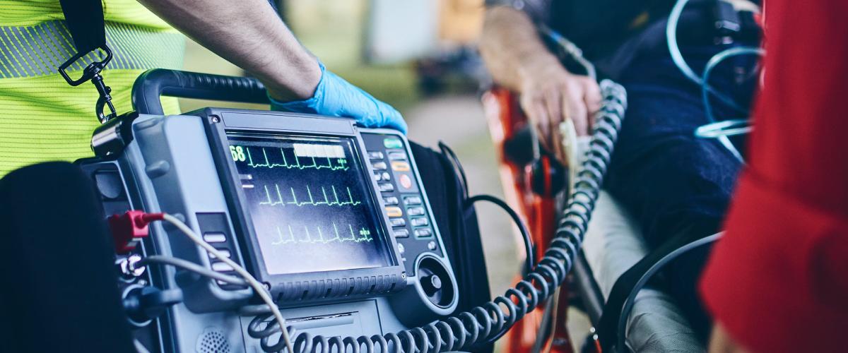 Paramedic holds heart monitor connected to person on stretcher.