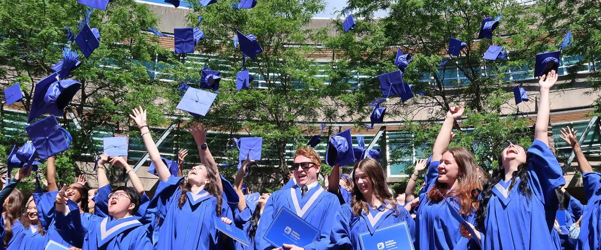 JIBC graduates in blue convocation gowns toss their caps in the air.