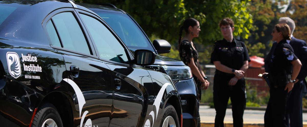 Black police car with Indigenous designs in white in foreground while four people, including two in police uniforms, stand in background.