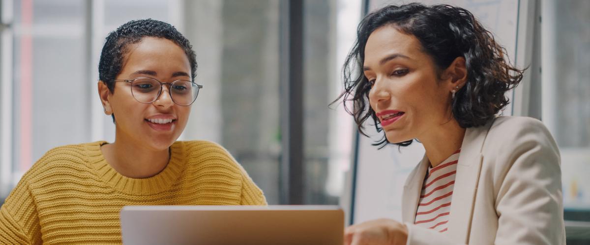 A woman gestures to a laptop screen while another woman looks on.