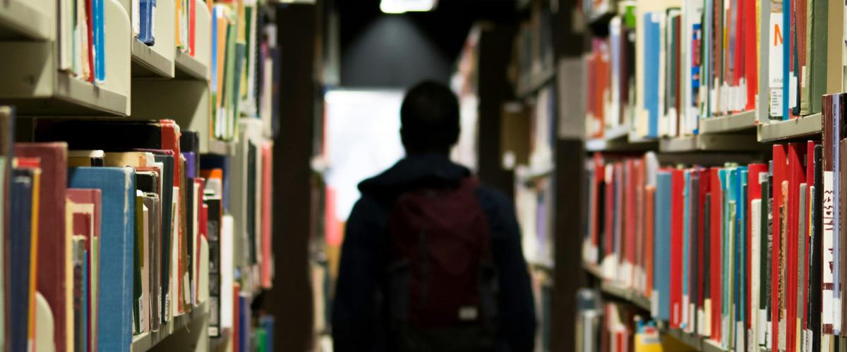 Person standing in middle of row of bookshelves.