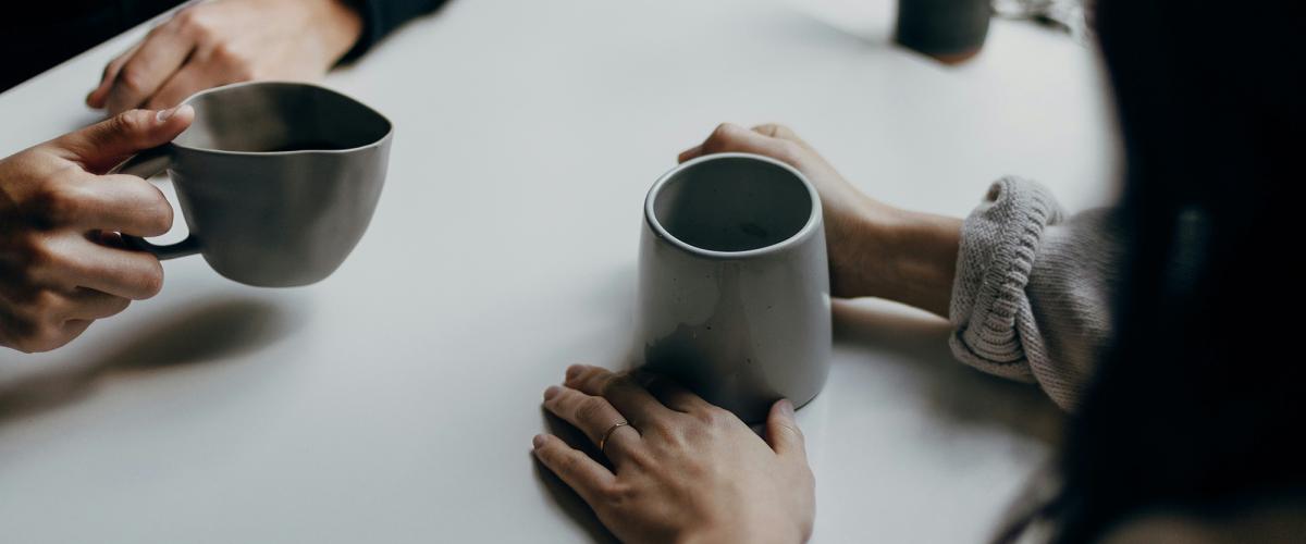 Two people site across a table holding mugs.