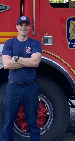FFTC grad Jesse Fryer in front of fire truck at JIBC Maple Ridge campus.