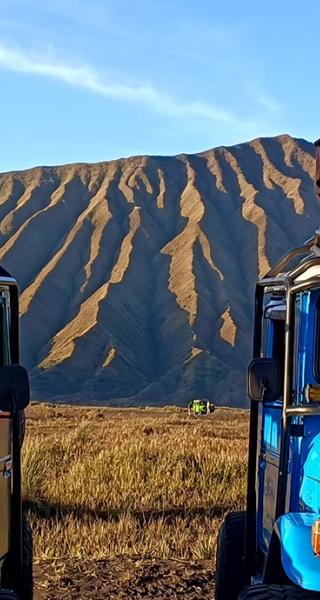 Four students sit atop jeeps with Indonesian mountains in background.