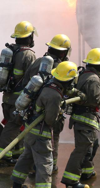 Group of firefighting students fighting fire while instructors look on.