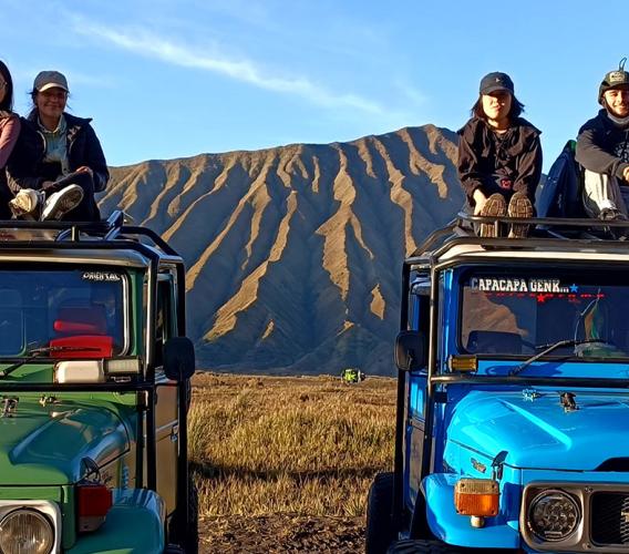 Four students sit atop jeeps with Indonesian mountains in background.