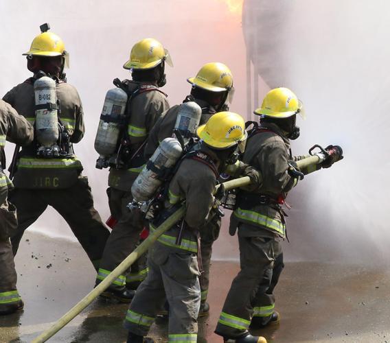 Group of firefighting students fighting fire while instructors look on.