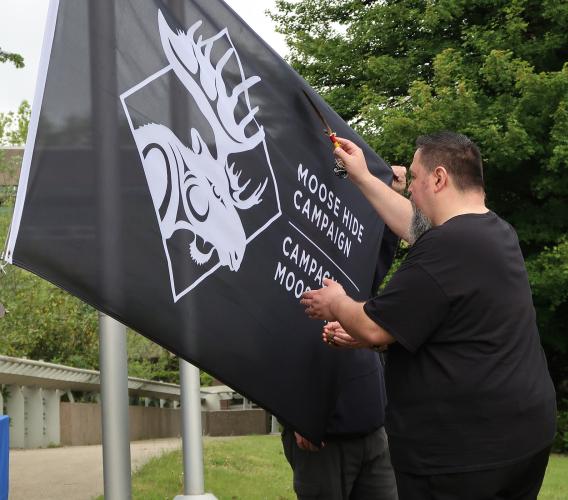 Man waves feather over a black flag with an image of a moose that says, "Moose Hide Campaign"
