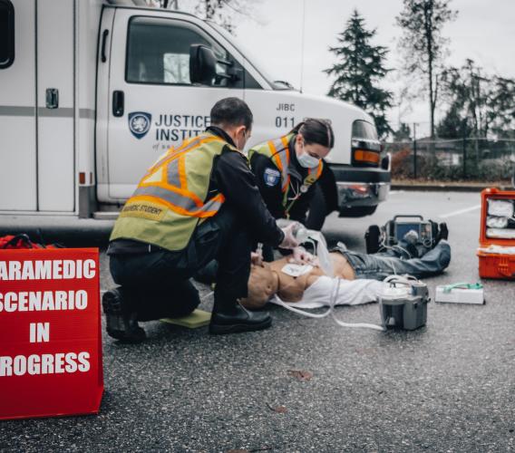 Two paramedic students work on a dummy on the pavement in a scenario training exercise.