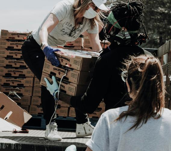 Woman passes crate of food to a man wearing gloves.