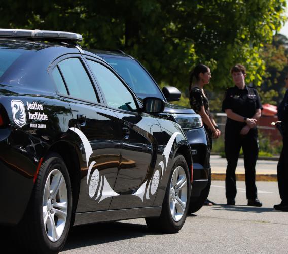 A group of four people stand in front of JIBC Police Academy vehicle with Indigenous artwork on the doors.