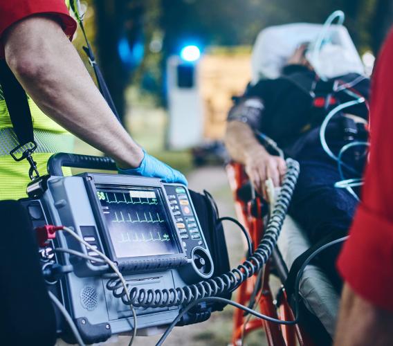 Paramedic holds heart monitor connected to person on stretcher.