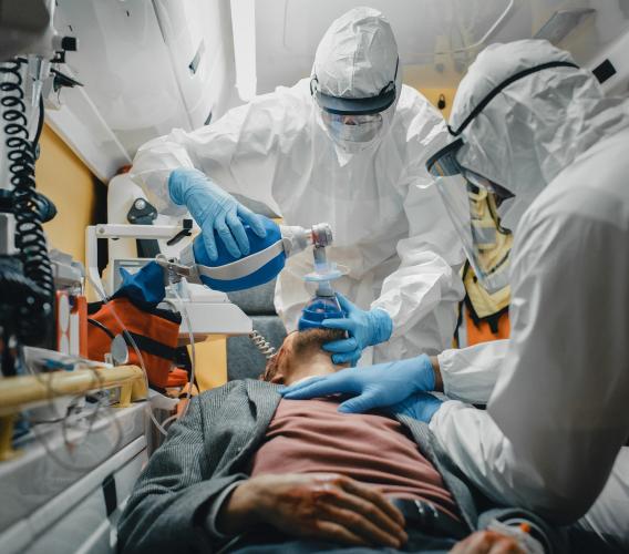 Two paramedics in full personal protective equipment work on a patient in an ambulance.