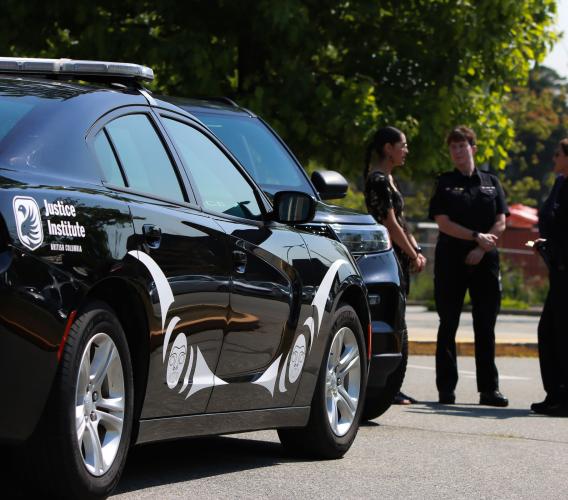 Black police car with Indigenous designs in white in foreground while four people, including two in police uniforms, stand in background.