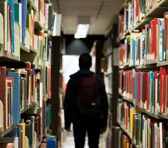 Person standing in middle of row of bookshelves.