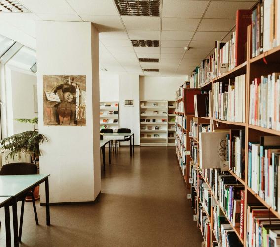 Room with bookshelves on right and tables and chairs by windows on left. 