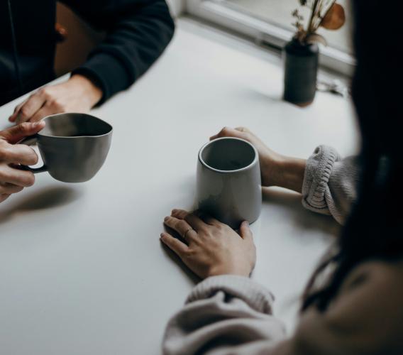 Two people site across a table holding mugs.