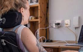 Woman with head in headrest of motorized wheelchair works on laptop.